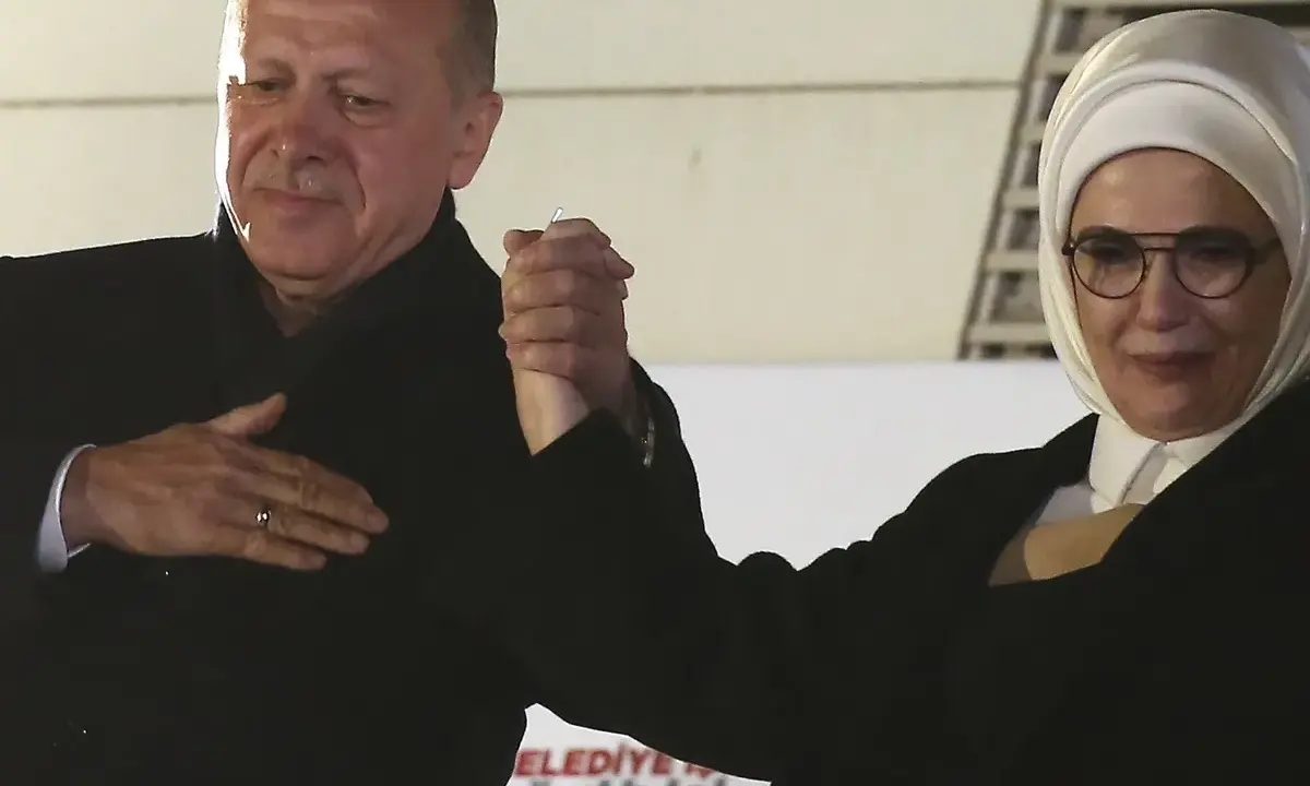 Erdogan und seine Frau, die ein Kopftuch trägt, halten Händchen.
