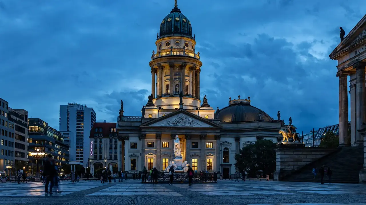 Der Gendarmenmarkt in Berlin bei Dämmerung. Die Kuppeln des Deutschen und Französischen Doms, Zeugen der Hugenotten in Berlin, erstrahlen im Licht.