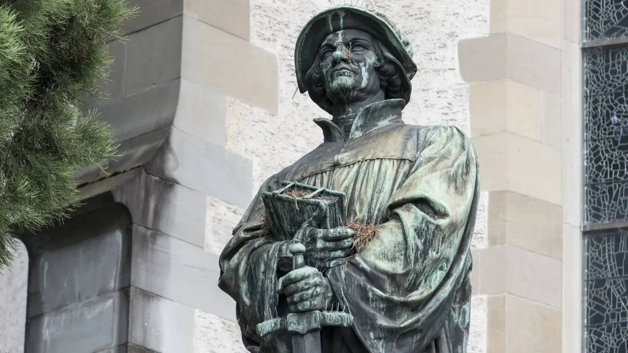 Bronzestatue von Huldrych Zwingli mit Buch und Schwert, ein Symbol für seinen Glauben und Kampf.