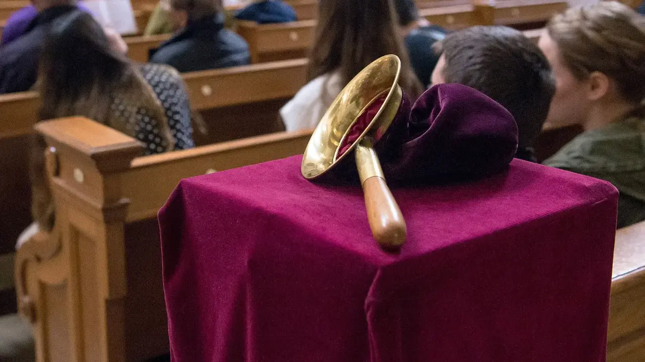 Gabe beim Gottesdienst: Eine Glocke auf einem mit Samt bezogenen Tisch, während Gläubige in den Kirchenbänken sitzen.