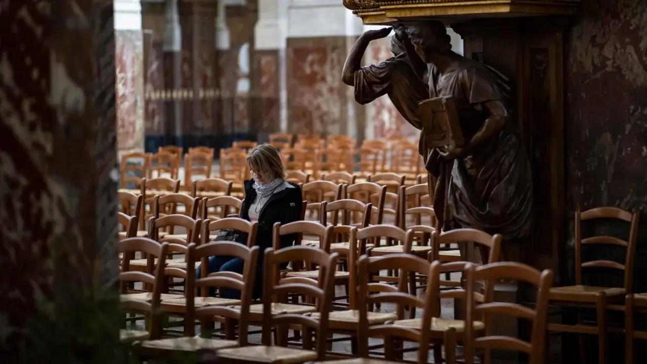 Frau sitzt allein in einer leeren Kirche, umgeben von Stuhlreihen. Eine Statue wacht über sie. Ein Moment der Stille, vielleicht ein Gebet oder eine Reflexion, bevor die "la cimade" beginnt.