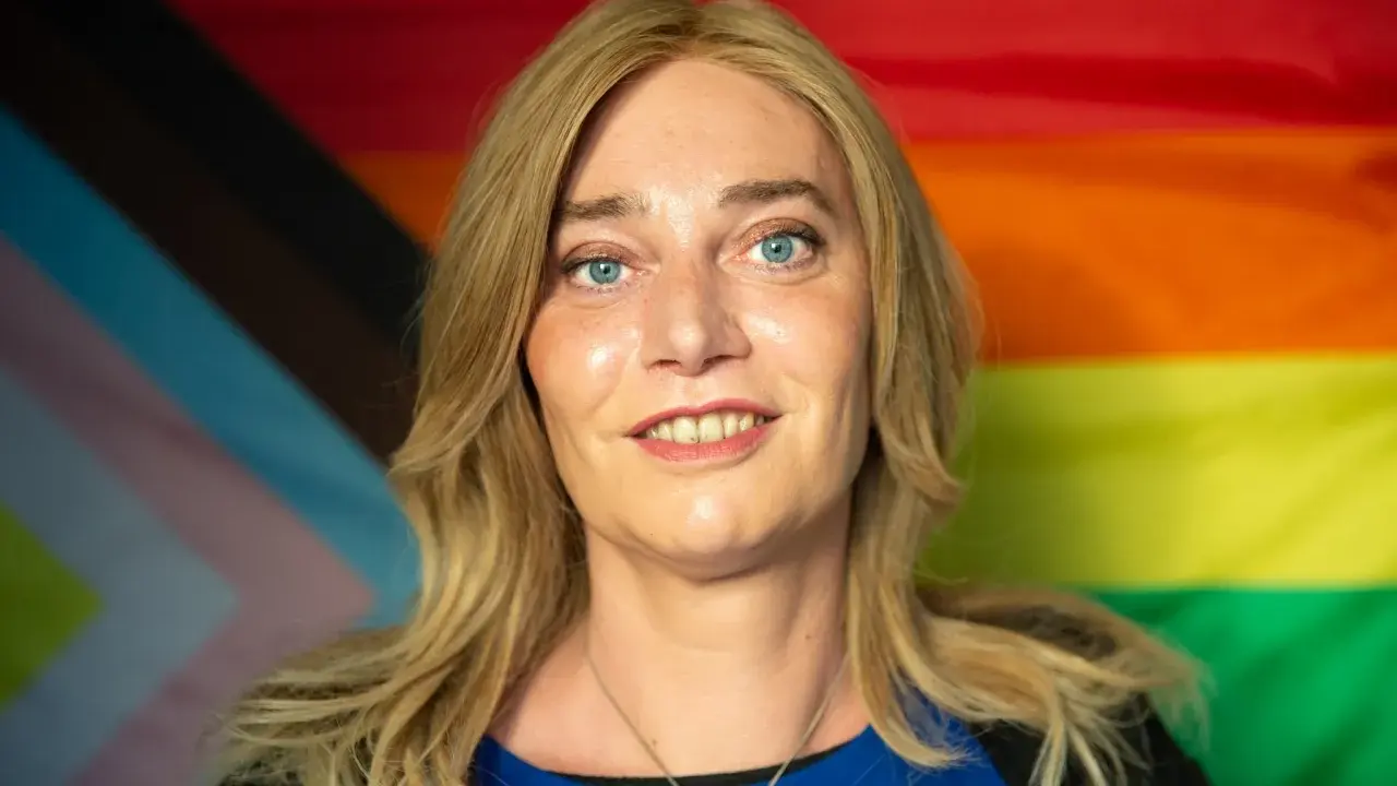 Markus Ganserer lächelt vor einer Pride-Flagge.