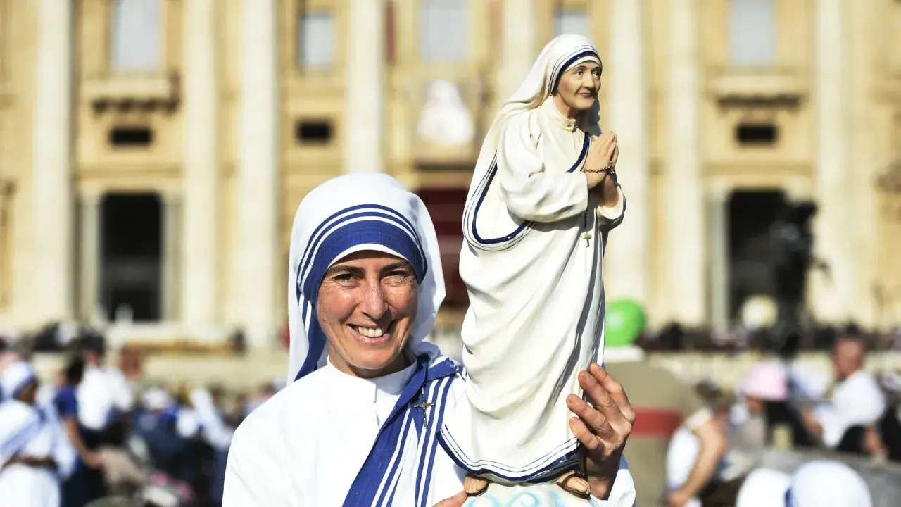 Eine Frau im Habit von Mutter Teresa hält eine Statue von ihr. Sie zeigt, was Mutter Teresa gemacht hat: Nächstenliebe und Hilfe für Bedürftige.