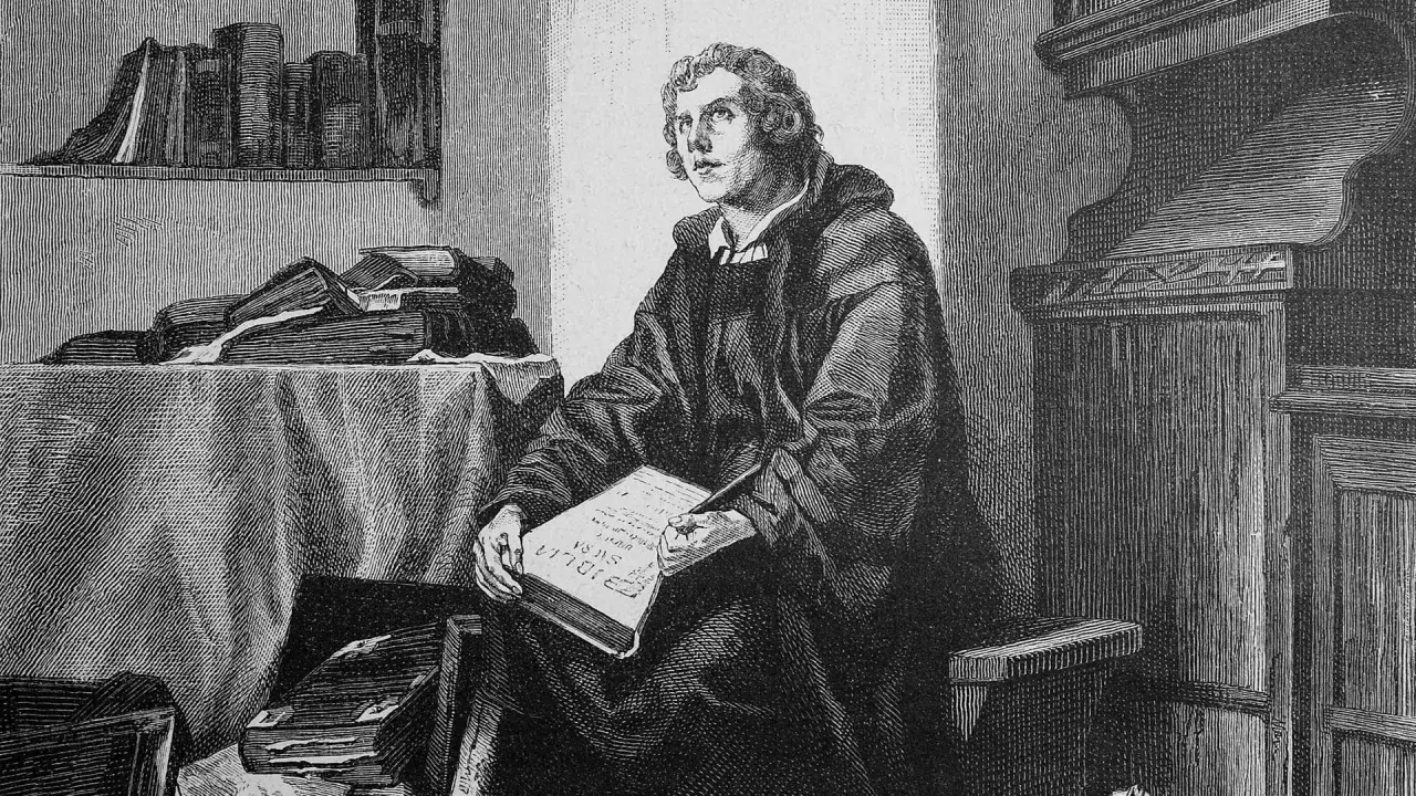 Martin Luther sitzt in seinem Studierzimmer und schreibt an seiner Bibelübersetzung. Bücher stapeln sich um ihn herum.