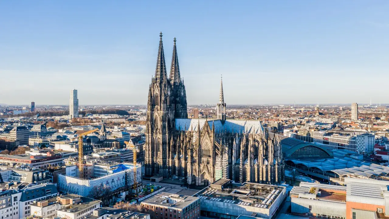 Majestätische gotische Kirchen ragen über einer Stadt auf. Der Kölner Dom, ein Meisterwerk gotischer Architektur, dominiert die Skyline.