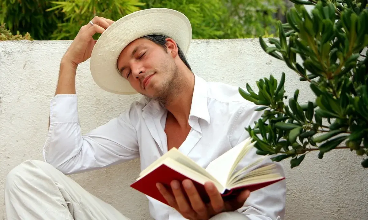 Ein Mann in weißem Hemd und Hut liest ein Buch, genießt die Ruhe. Er verkörpert, was sind Hedonisten: Menschen, die das Leben und seine Freuden suchen.