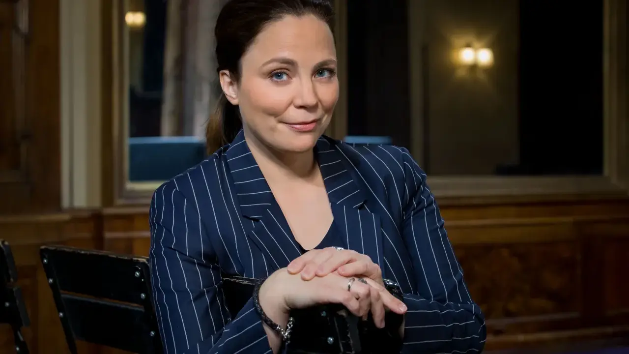 Karen Duve macht eine nachdenkliche Miene, während sie in einem gestreiften Blazer sitzt.