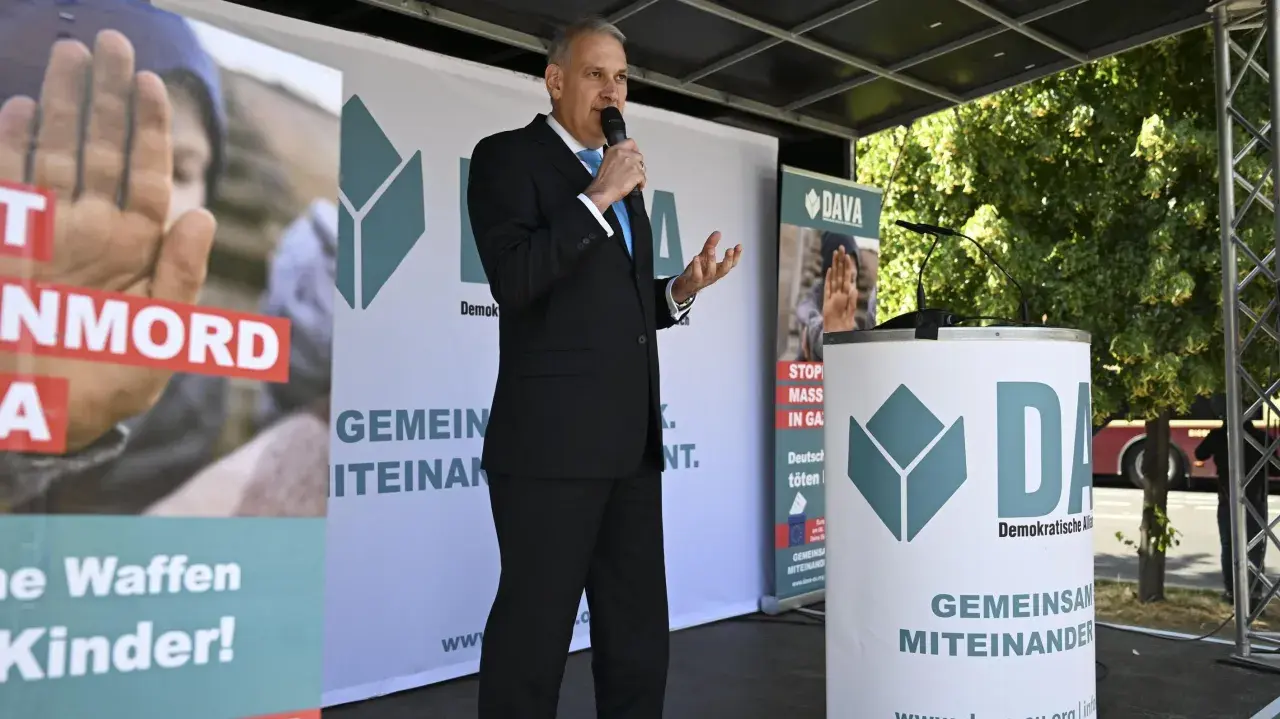 Mann spricht ins Mikrofon vor DAVA-Banner. "Gemeinsam Miteinander" steht auf den Bannern.