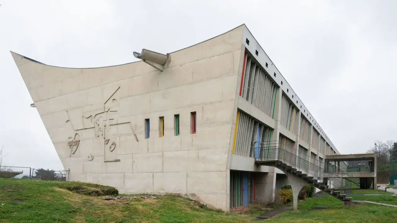 Betonbau mit bunten Fenstern und einer markanten, geschwungenen Form. Ein Meisterwerk des Architekten Le Corbusier.