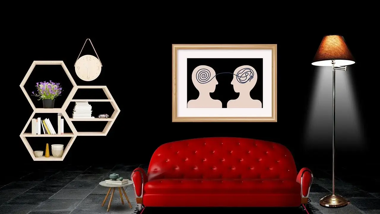 Ein rotes Sofa vor einem Bild, das zwei Köpfe mit verschlungenen Linien zeigt, symbolisiert die Seele. Ein Regal mit Büchern und eine Lampe vervollständigen die Szene.