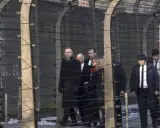 Eine Gruppe von Menschen, darunter ein Mann in einem langen schwarzen Mantel, geht hinter Stacheldraht entlang. Die Szene erinnert an die Verfolgung von Dietrich Bonhoeffer.