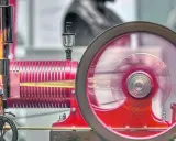 Eine funktionierende Denis Papin Dampfmaschine mit rot glühendem Kessel und einem sich drehenden Schwungrad.