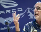 Philip Nitschke spricht mit erhobener Hand vor einem blauen Hintergrund mit dem SARCO-Logo.