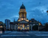 Der Gendarmenmarkt in Berlin bei Dämmerung. Die Kuppeln des Deutschen und Französischen Doms, Zeugen der Hugenotten in Berlin, erstrahlen im Licht.