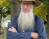 Ein älterer Amish-Mann mit langem, weißem Bart und Strohhut blickt nachdenklich.