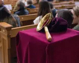Gabe beim Gottesdienst: Eine Glocke auf einem mit Samt bezogenen Tisch, während Gläubige in den Kirchenbänken sitzen.