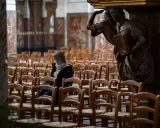 Frau sitzt allein in einer leeren Kirche, umgeben von Stuhlreihen. Eine Statue wacht über sie. Ein Moment der Stille, vielleicht ein Gebet oder eine Reflexion, bevor die "la cimade" beginnt.