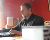 Mann arbeitet am Laptop im Büro des Antaios Verlags. Bücherregale im Hintergrund.