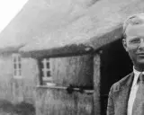 Ein Mann mit Brille steht vor einem Reetdachhaus. Er ist Dietrich Bonhoeffer, ein deutscher Theologe und Widerstandskämpfer.
