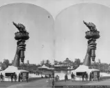 Die Hand mit der Fackel der Freiheitsstatue, ein Werk der freiheitsstatue erbauer, ragt über einem Pavillon auf. Im Hintergrund ist eine Parklandschaft mit einem See und Gebäuden zu sehen.