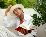 Ein Mann in weißem Hemd und Hut liest ein Buch, genießt die Ruhe. Er verkörpert, was sind Hedonisten: Menschen, die das Leben und seine Freuden suchen.