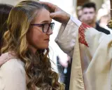Ein Bischof legt einer jungen Frau die Hand auf die Stirn. Sie hat lange, blonde Haare und trägt eine Brille. Dies ist ein Moment, in dem sie ihren Glauben an Gott bekräftigt.