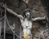 Skulptur Jesu am Kreuz, die an die Frage erinnert, warum wurde Jesus gekreuzigt. Die Darstellung ist durch ein Gitter geschützt.