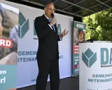 Mann spricht ins Mikrofon vor DAVA-Banner. "Gemeinsam Miteinander" steht auf den Bannern.
