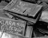 Stapel von alten Koffern, beschriftet mit Namen wie "Klara Goldstein" und "Kind Weissbrod Johanna". Diese Auschwitz Koffer sind ein trauriges Zeugnis der Vergangenheit.