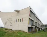 Betonbau mit bunten Fenstern und einer markanten, geschwungenen Form. Ein Meisterwerk des Architekten Le Corbusier.