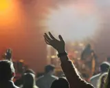 Eine Hand hebt sich im Scheinwerferlicht, während eine Menge bei einem Konzert jubelt. Dies spiegelt die lebendige Pfingstler Erziehung wider, die Gemeinschaft und Ausdruck fördert.