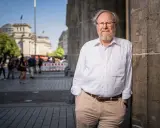 Wolfgang Thierse, lächelnd, lehnt an einer Säule vor dem Reichstagsgebäude in Berlin.