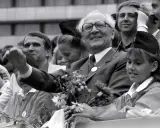 Ein Mann mit Brille winkt lächelnd, umgeben von Menschen. War die DDR eine Diktatur? Diese Szene zeigt eine öffentliche Veranstaltung, vielleicht ein Zeichen der Hoffnung.