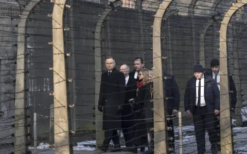 Eine Gruppe von Menschen, darunter ein Mann in einem langen schwarzen Mantel, geht hinter Stacheldraht entlang. Die Szene erinnert an die Verfolgung von Dietrich Bonhoeffer.
