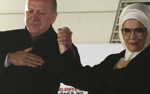 Erdogan und seine Frau, die ein Kopftuch trägt, halten Händchen.