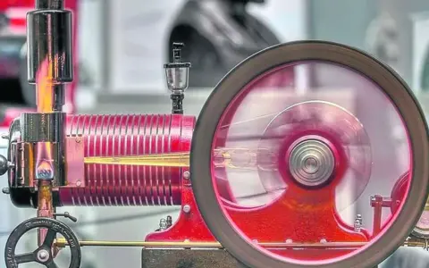 Eine funktionierende Denis Papin Dampfmaschine mit rot glühendem Kessel und einem sich drehenden Schwungrad.