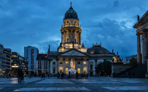 Der Gendarmenmarkt in Berlin bei Dämmerung. Die Kuppeln des Deutschen und Französischen Doms, Zeugen der Hugenotten in Berlin, erstrahlen im Licht.