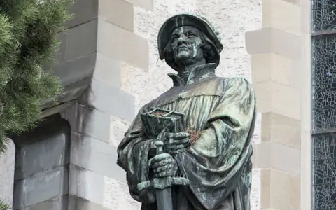 Bronzestatue von Huldrych Zwingli mit Buch und Schwert, ein Symbol für seinen Glauben und Kampf.