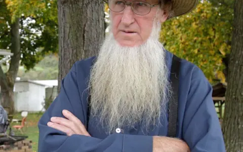 Ein älterer Amish-Mann mit langem, weißem Bart und Strohhut blickt nachdenklich.