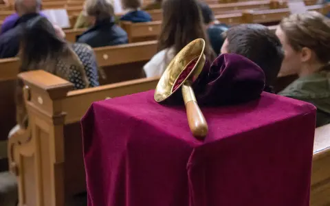 Gabe beim Gottesdienst: Eine Glocke auf einem mit Samt bezogenen Tisch, während Gläubige in den Kirchenbänken sitzen.
