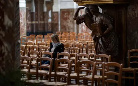 Frau sitzt allein in einer leeren Kirche, umgeben von Stuhlreihen. Eine Statue wacht über sie. Ein Moment der Stille, vielleicht ein Gebet oder eine Reflexion, bevor die "la cimade" beginnt.