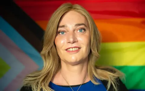 Markus Ganserer lächelt vor einer Pride-Flagge.