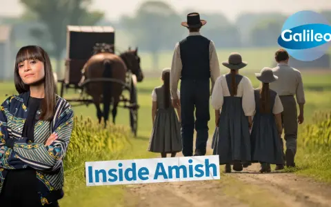Eine Frau blickt in die Kamera, während im Hintergrund eine Amish-Familie mit Pferdekutsche auf einem Feldweg geht.