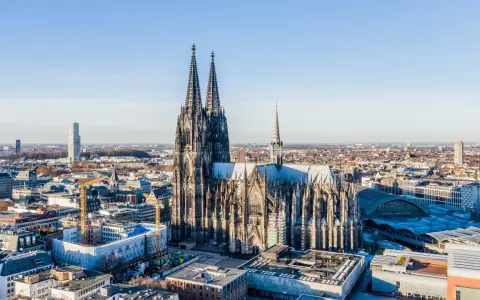 Majestätische gotische Kirchen ragen über einer Stadt auf. Der Kölner Dom, ein Meisterwerk gotischer Architektur, dominiert die Skyline.