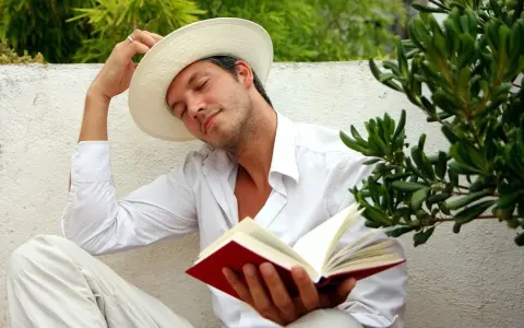 Ein Mann in weißem Hemd und Hut liest ein Buch, genießt die Ruhe. Er verkörpert, was sind Hedonisten: Menschen, die das Leben und seine Freuden suchen.