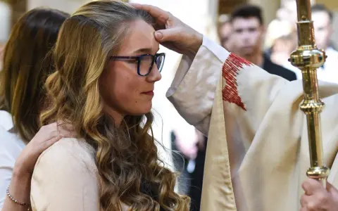 Ein Bischof legt einer jungen Frau die Hand auf die Stirn. Sie hat lange, blonde Haare und trägt eine Brille. Dies ist ein Moment, in dem sie ihren Glauben an Gott bekräftigt.
