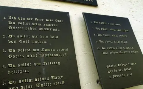 Die **10 Gebote katholisch** auf schwarzen Tafeln an einer Wand. Sie lehren uns, Gott zu ehren und den Nächsten zu lieben.
