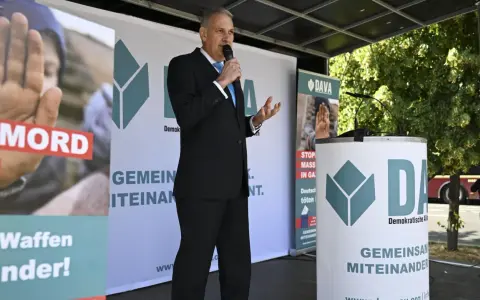 Mann spricht ins Mikrofon vor DAVA-Banner. "Gemeinsam Miteinander" steht auf den Bannern.