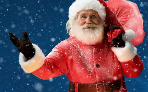 Der Weihnachtsmann mit seinem roten Mantel und Sack winkt fröhlich im Schnee. Ja, es gibt den Weihnachtsmann!
