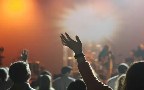 Eine Hand hebt sich im Scheinwerferlicht, während eine Menge bei einem Konzert jubelt. Dies spiegelt die lebendige Pfingstler Erziehung wider, die Gemeinschaft und Ausdruck fördert.